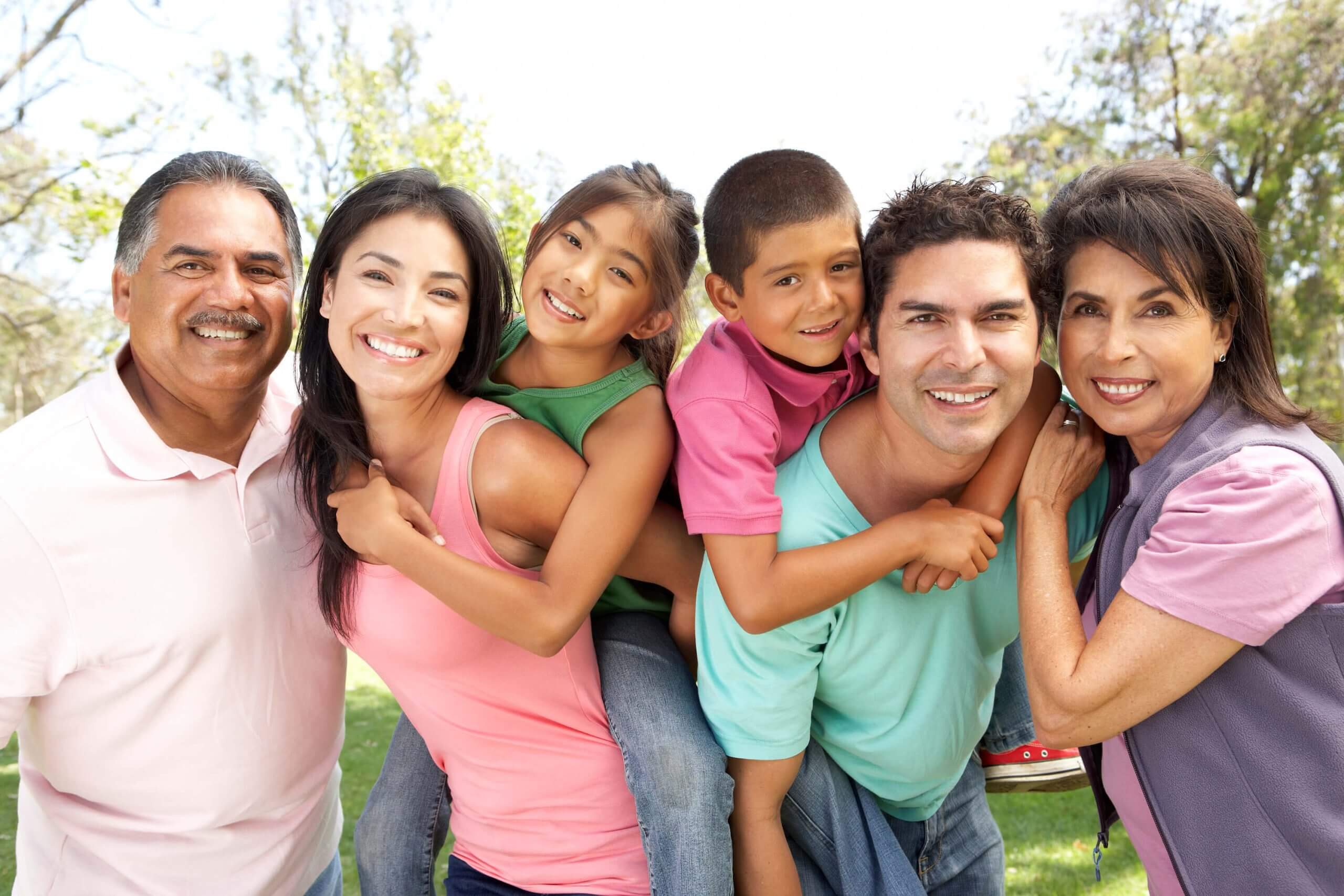 extended multi-cultural family posing in a park and smiling at the camera